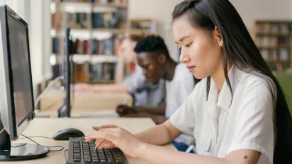 Woman and man working on a computer in a library setting.