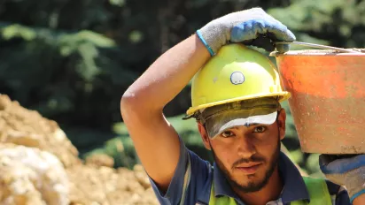 A construction worker with a hard hat, carrying bucket of cement on his shoulder