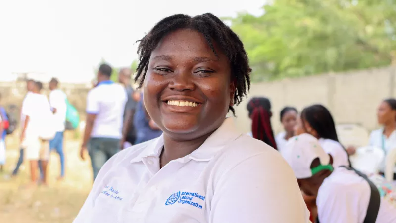 A young African women wearing an ILO shirt is looking at the camera and smiling in Abidjan, Côte d'Ivoire